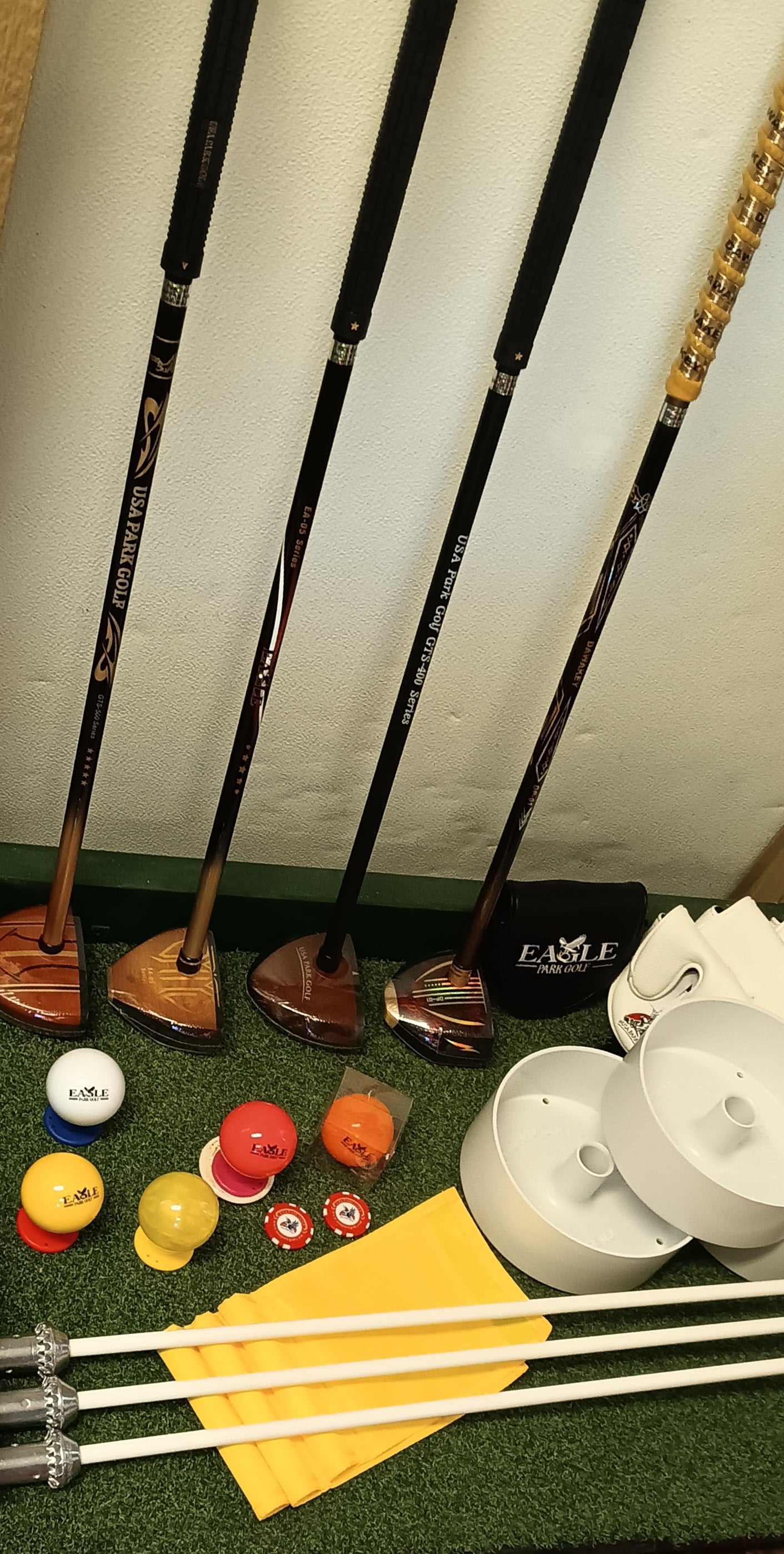 Collection of park golf clubs and park golf balls with flags and flag sticks.